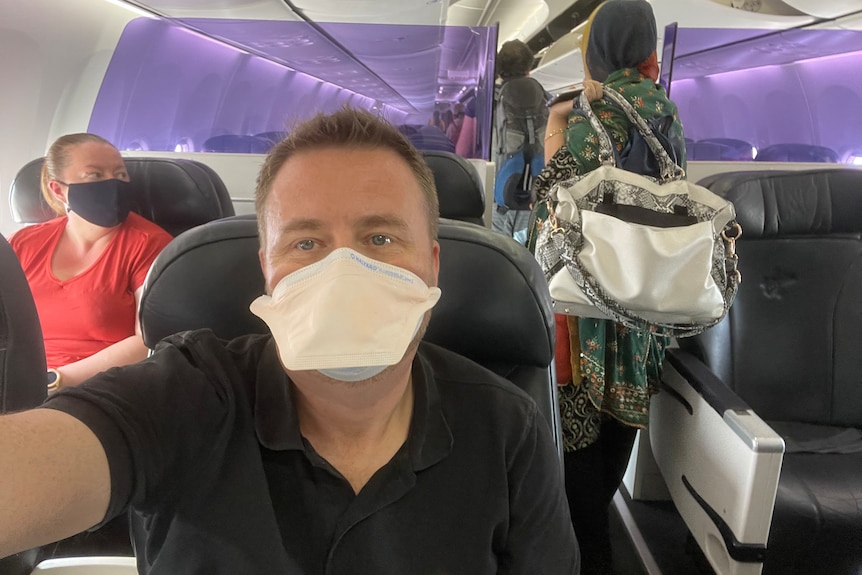 Man wearing mask takes selfie on plane.