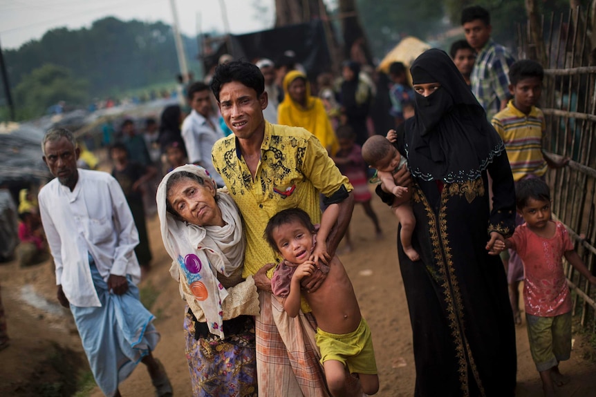 A man helps an elderly woman and a child along a path.