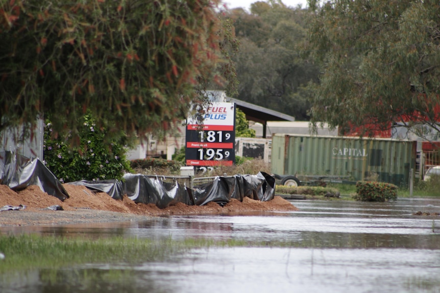 floodwaters approach a low levee of dirt and black plastic in front of a petrol station sign