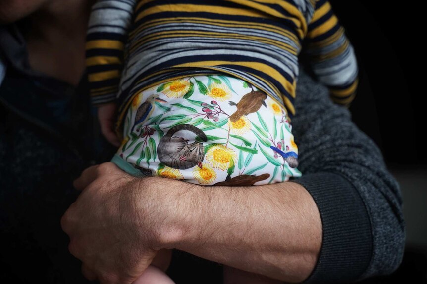 A man's arm wrapped around a baby.