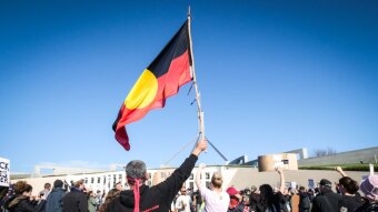 a person waves an indigenous flag in front of parliament house.