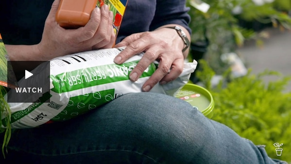 A person sitting with a bag of fertiliser on their lap and holding a bottle of liquid fertiliser. Has Video
