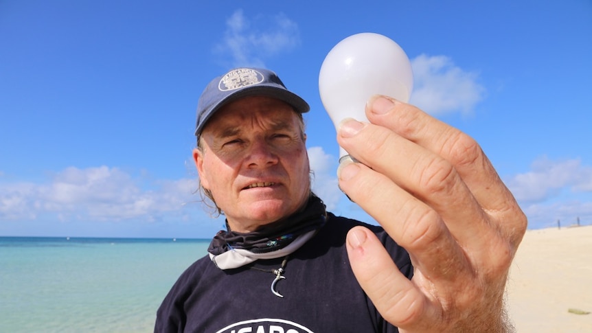 Matt Wheldon standing in the sand examining a light bulb he found on a far north Queensland island.