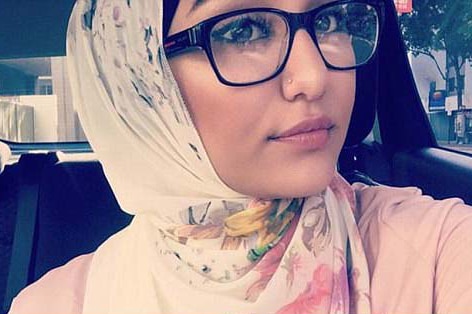 Aya poses for a selfie in a car, she wears a headscarf and nose stud.