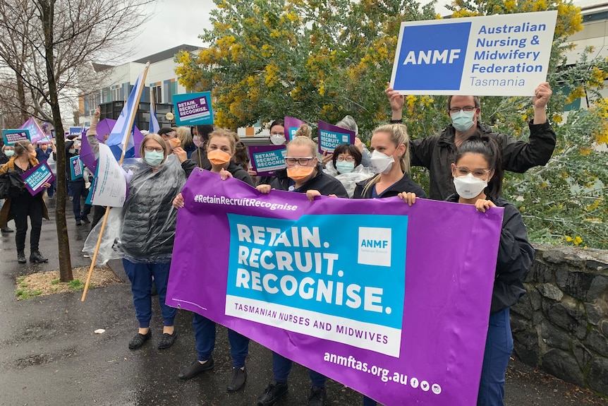 A group of nurses wearing masks hold signs on a sidewalk in Launceston.