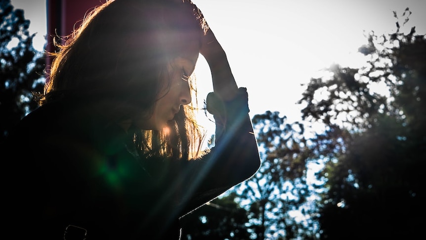 A stressed-looking woman holds her hand to her head