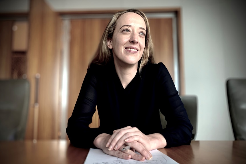 Beth Cameron sits at a board table, smiling, with a note pad in front of her.