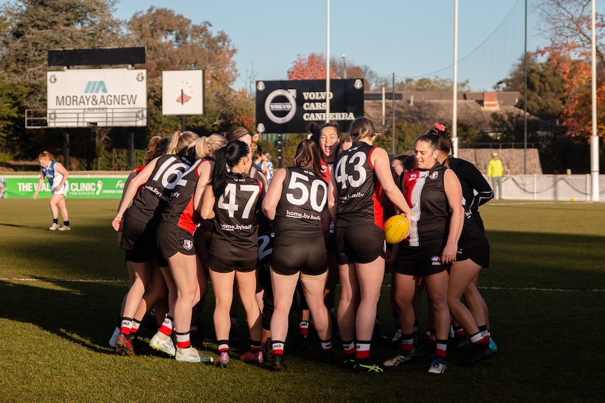 The Ainslie women's soccer team gathers in a group on the Australian rules ground.