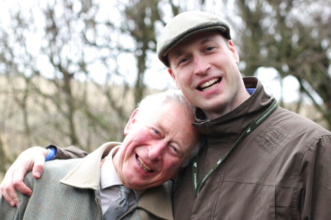 Prince Charles leans into Prince William as the pair look at the camera smiling.