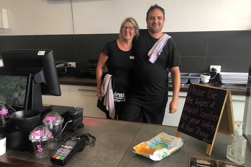 A man and woman stand behind a counter in a cafe.