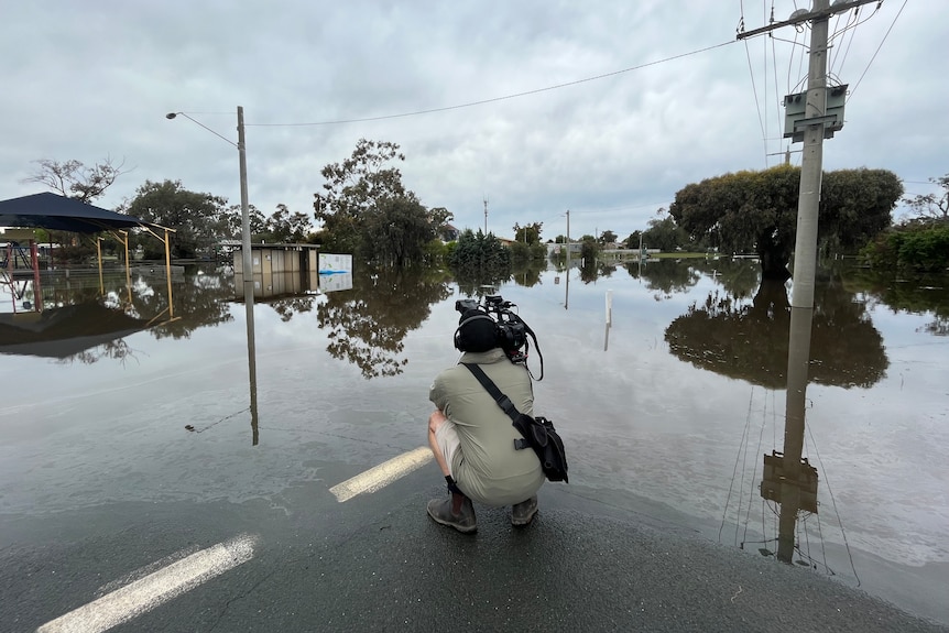 Cameraman crouching down while filming widely flooded street.