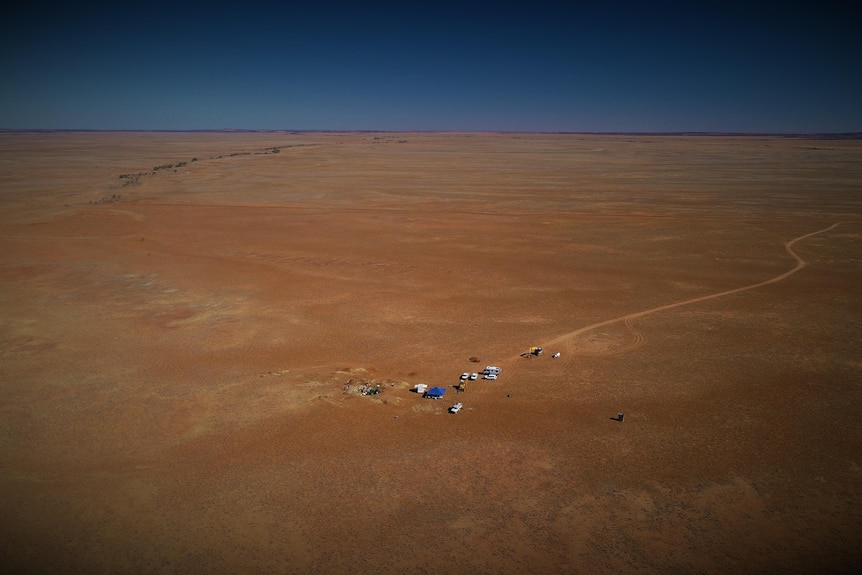 An aerial shot of dry, dusty red outback landscape with some tents and cars.