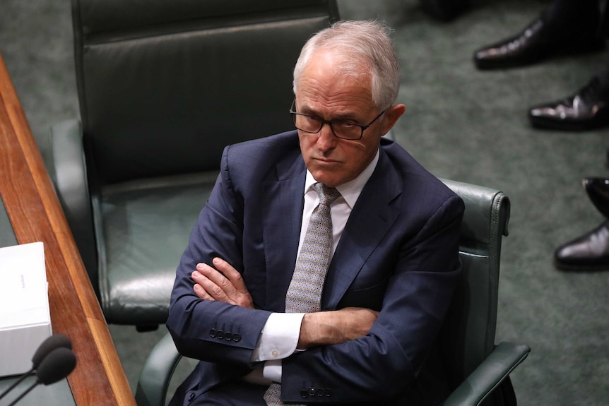Prime Minister Malcolm turnbull sits with crossed arms during Question Time. He's wearing a navy suit and glasses.
