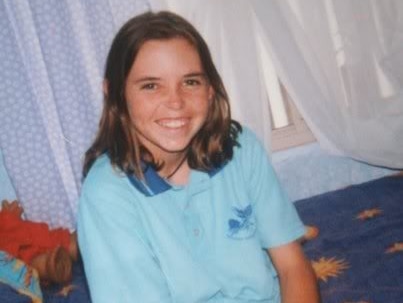 A smiling Hayley Dodd sits on a bed wearing a light blue school polo shirt.