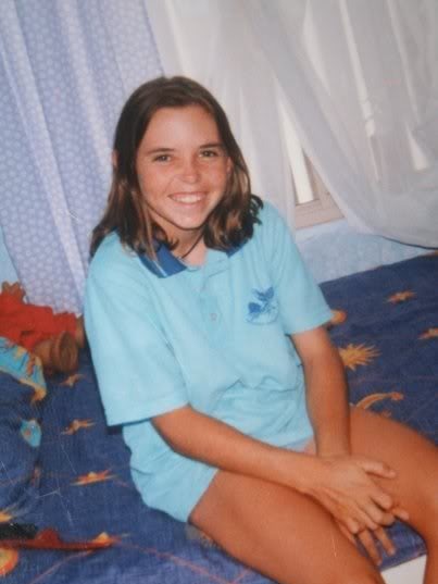 Un sourire Hayley Dodd est assis sur un lit vêtu d'un polo scolaire bleu clair.