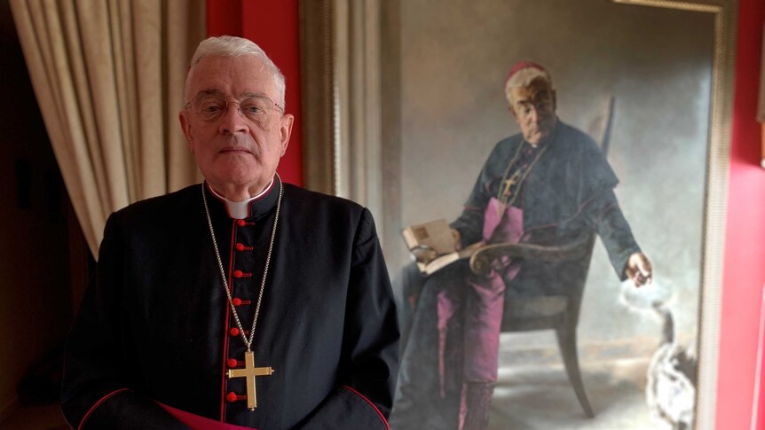 Bishop Peter Elliott, Auxiliary Bishop of Melbourne, standing in robes in front of a portrait of himself