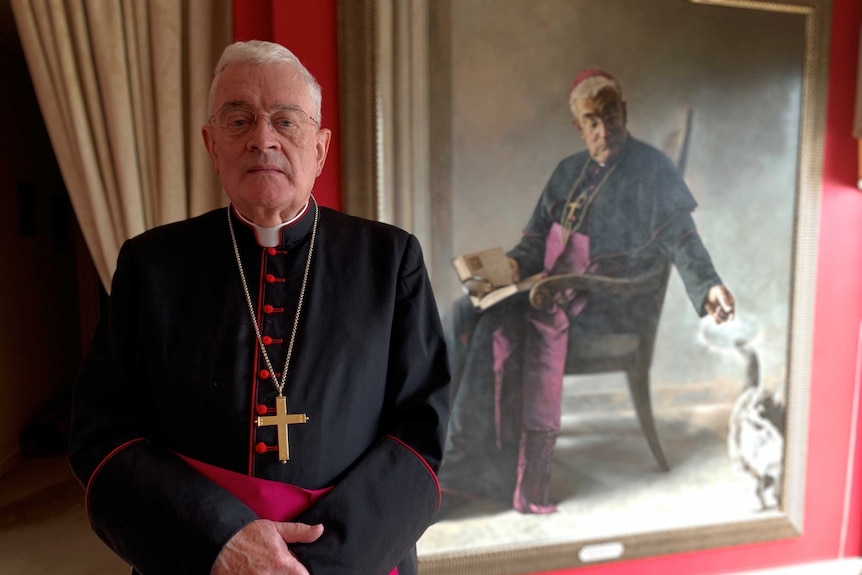 Bishop Peter Elliott, Auxiliary Bishop of Melbourne, standing in robes in front of a portrait of himself