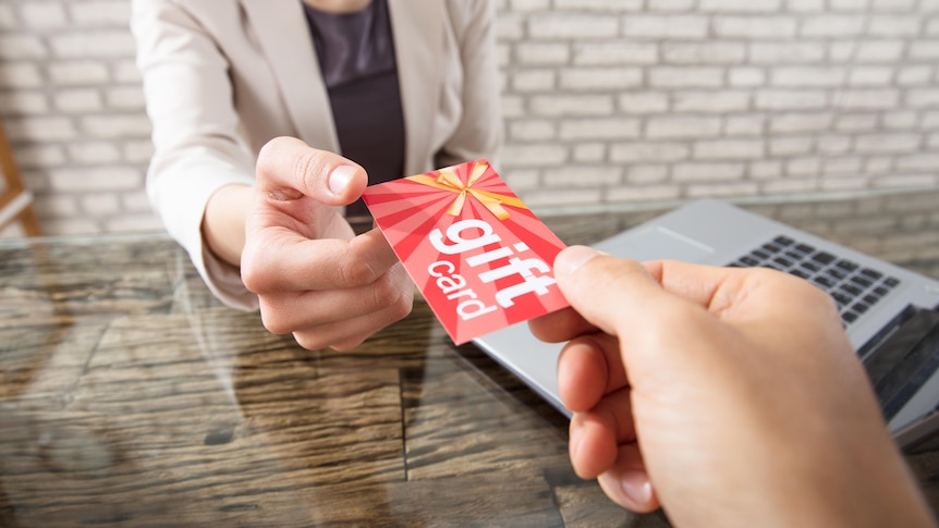 A close-up of a person's hand passing a gift card to another person.