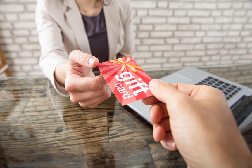 A close-up of a person's hand passing a gift card to another person.