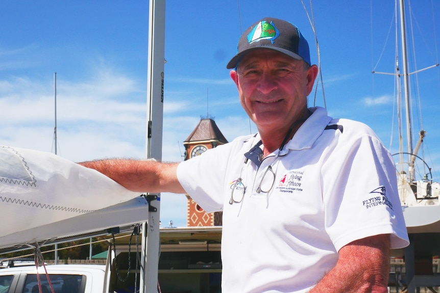 A man wearing a white polo t-shirt and cap stands next to a boat.