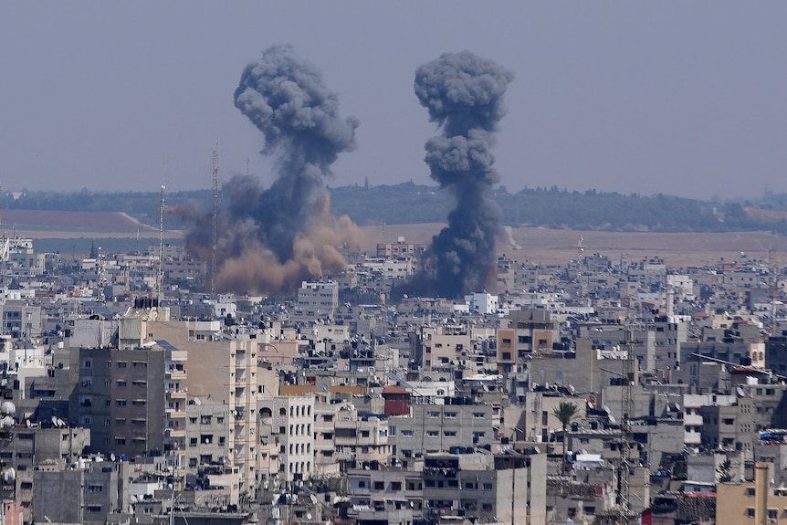 Dark grey smoke rises in two thick plumes from two buildings in the same section of Gaza.