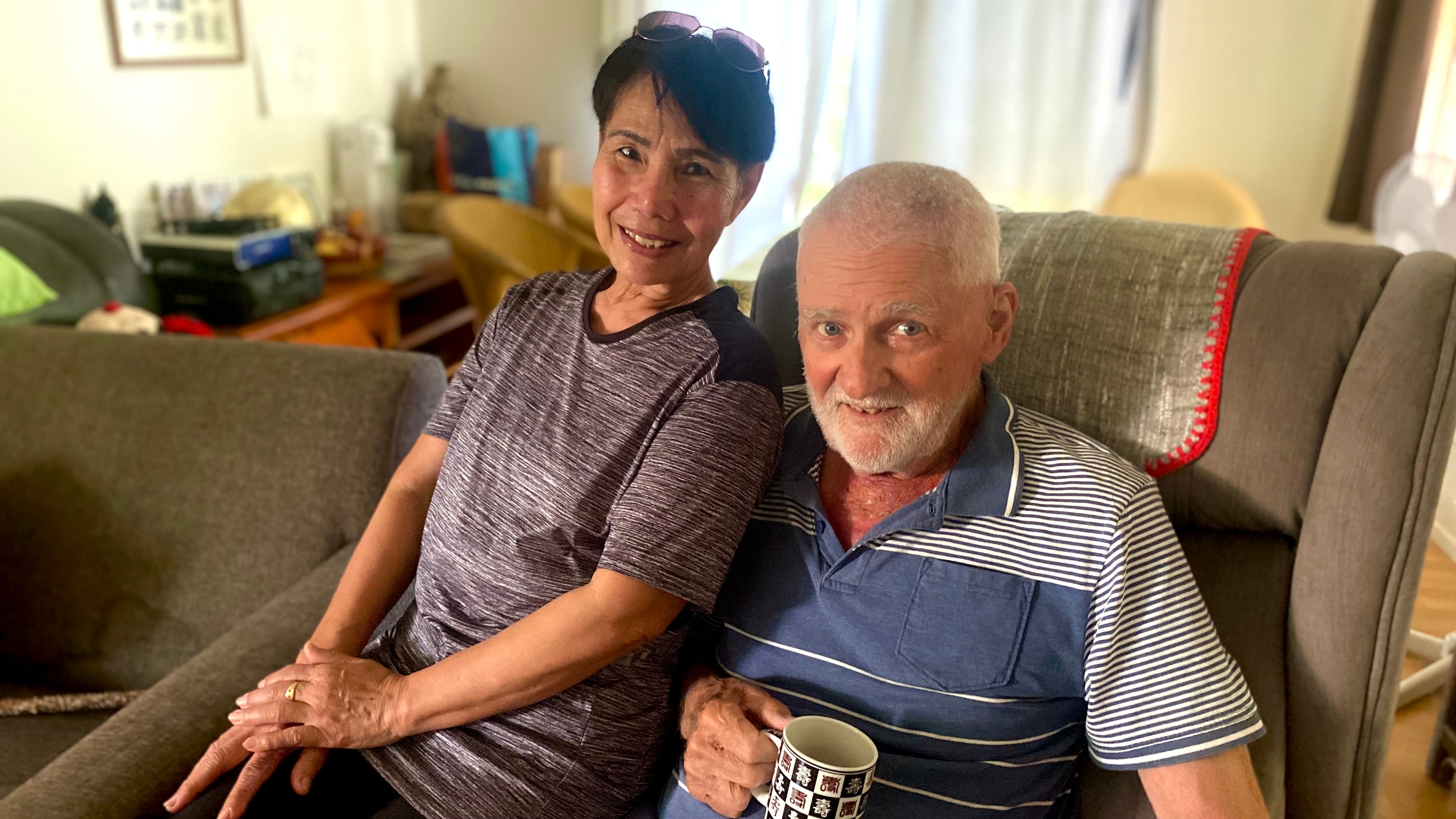 Adrian Ashenden sits next to his wife on an armchair in their home.