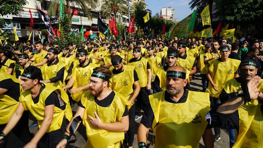 Hundreds of men wearing black and green headbands and yellow vests march in a parade.