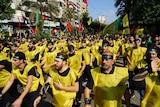Hundreds of men wearing black and green headbands and yellow vests march in a parade.