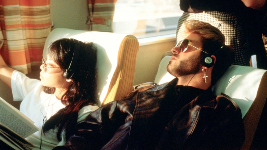 George Michael and girlfriend listening to music via earphones on a plane.