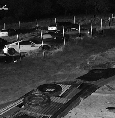 CCTV footage of a car yard, in the distance a hooded figure moves past cars