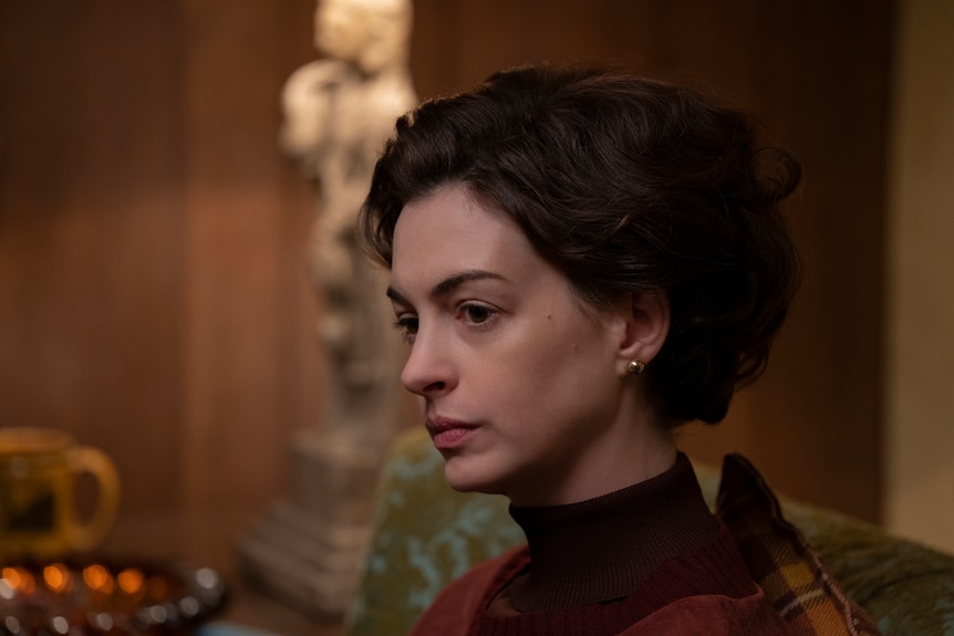 White woman with short brunette hair wears a red long-sleeved shirt and sits looking despondent at a dinner table.