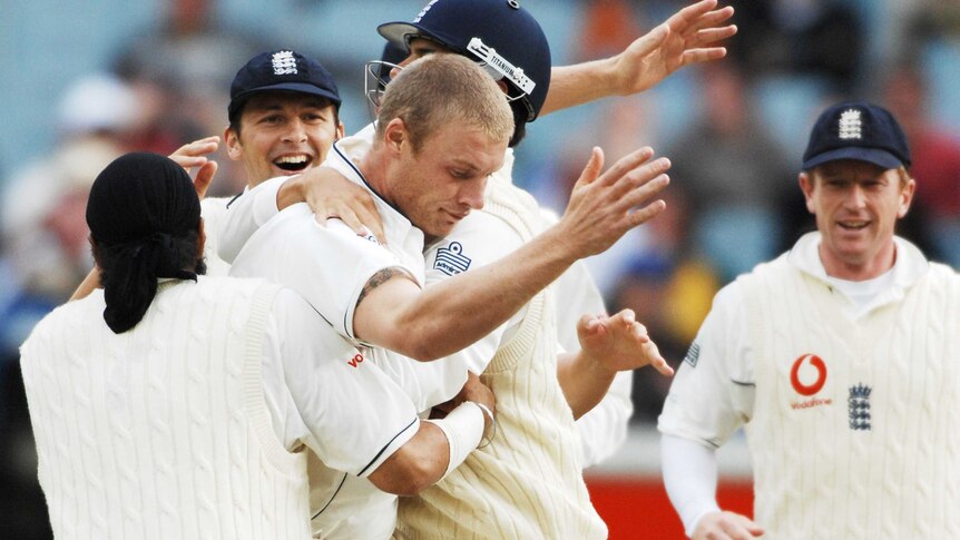 Andrew Flintoff holds his arms in the air with his head bowed as he is mobbed by teammates during the MCG Test.