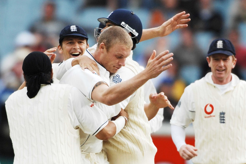 Andrew Flintoff holds his arms in the air with his head bowed as he is mobbed by teammates during the MCG Test.