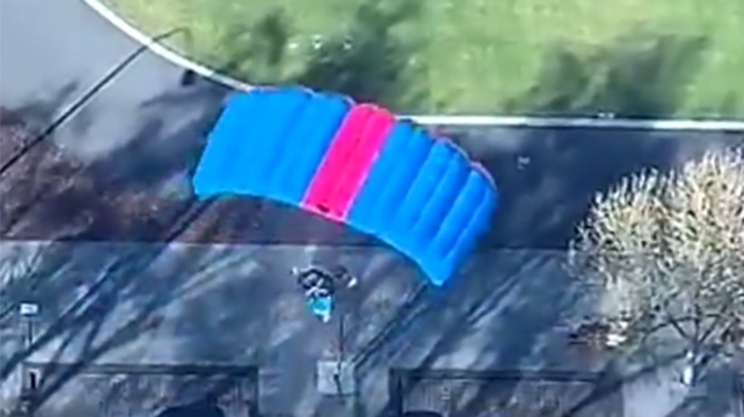 A person in a parachute in front of a tall building.