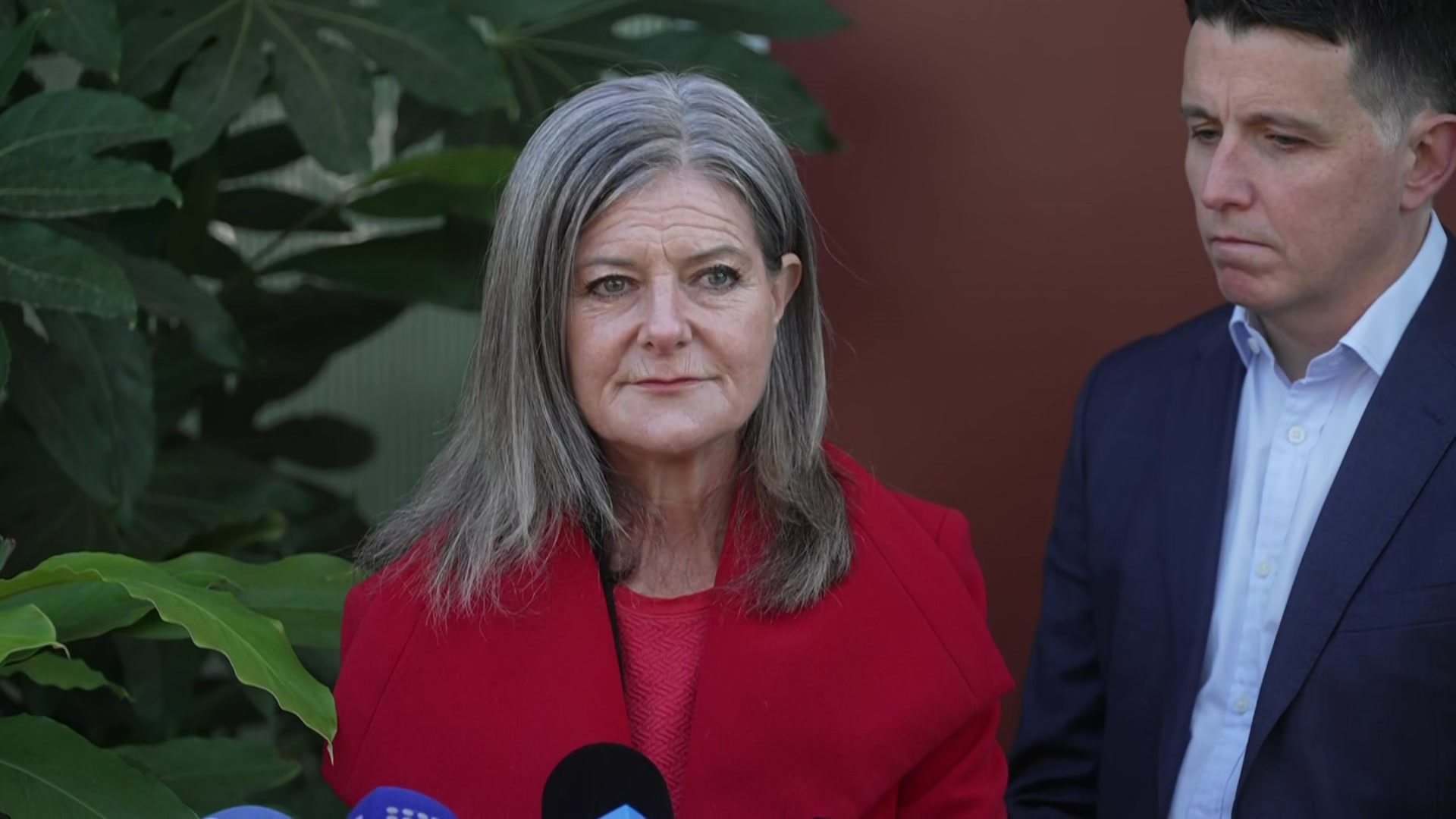 Una mujer con una chaqueta roja brillante se encuentra frente a los micrófonos de los medios.