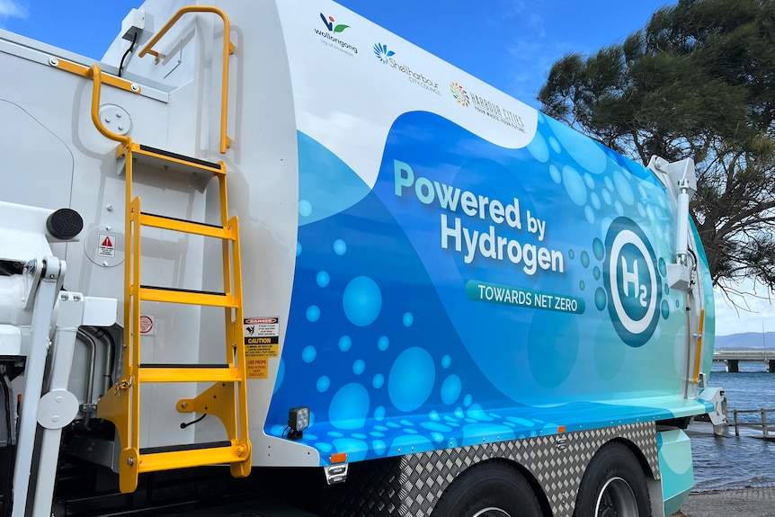 The exterior of the blue and white hydrogen-powered garbage truck and yellow ladder up the side.