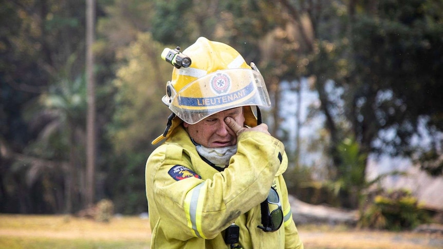 A fire lieutenant dressed in high vis wipes ash from his eyes.