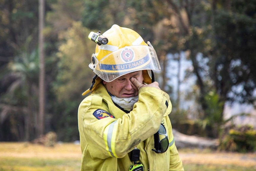 A fire lieutenant dressed in high vis wipes ash from his eyes.