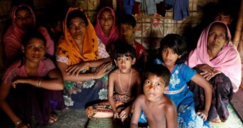 A group of people, including women and children, sit huddled together in a dark room.