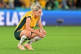 A soccer player wearing yellow and green sits on her haunches after a game