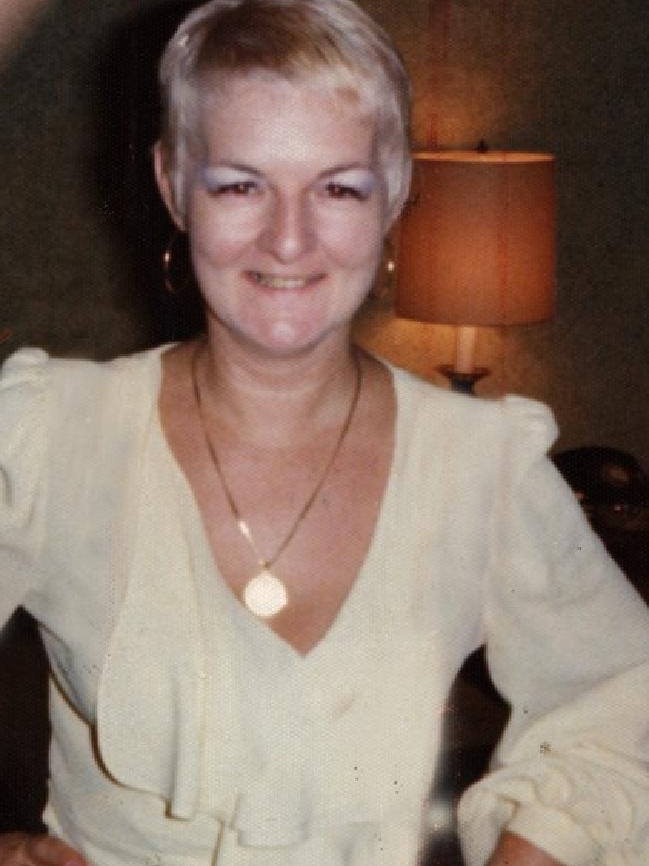 Shirley Finn stands with her hands on her hips in a white dress smiling for the camera.