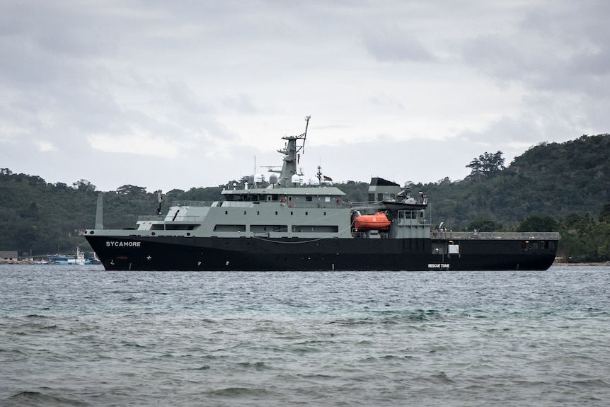 The left side of a warship on the ocean with dark stormy skies int he background