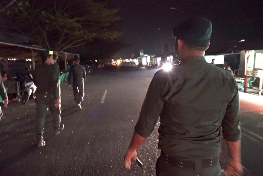 Aceh police walking along the median strip of a road in Aceh