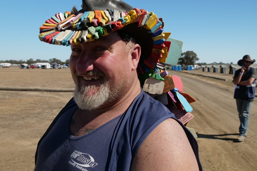 A man in a blue singlet and a decorated leather cowboy hat smiles