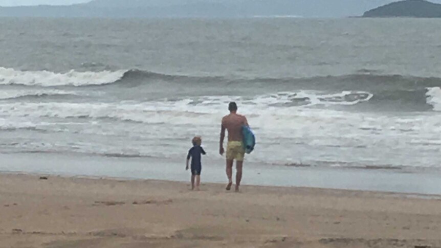 a man and a child walking into small surf at a beach