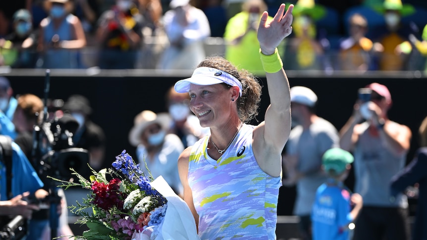 An Australian female tennis player waves to the Melbourne Park crowd holding a bunch of flowers.