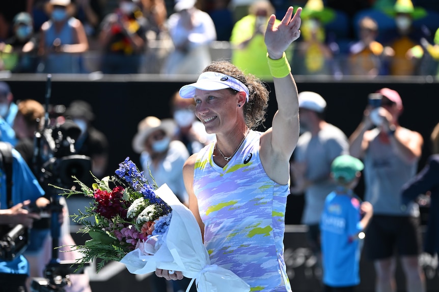 An Australian female tennis player waves to the Melbourne Park crowd holding a bunch of flowers.