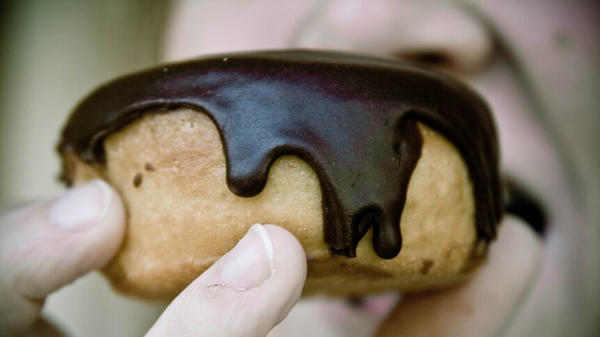 close up of chocolate glazed donut - man biting into donut