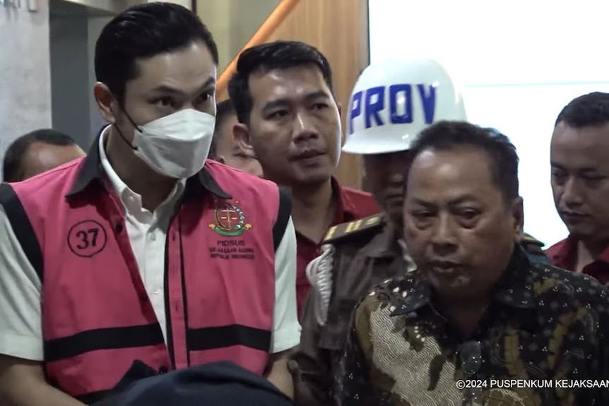 Harvey Moeis wearing a pink vest and a white face mask is escorted by Indonesia police.