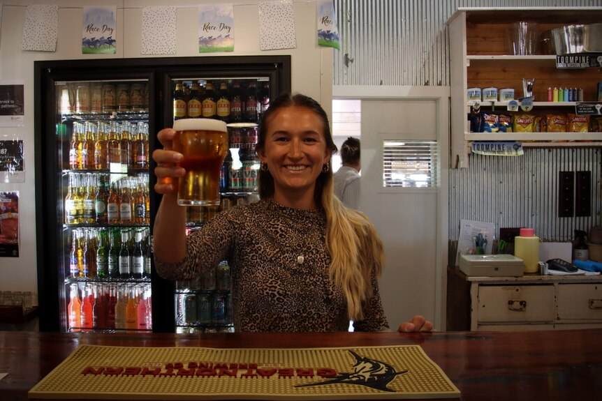 A young woman with blond hair is holding a beer at the bar.